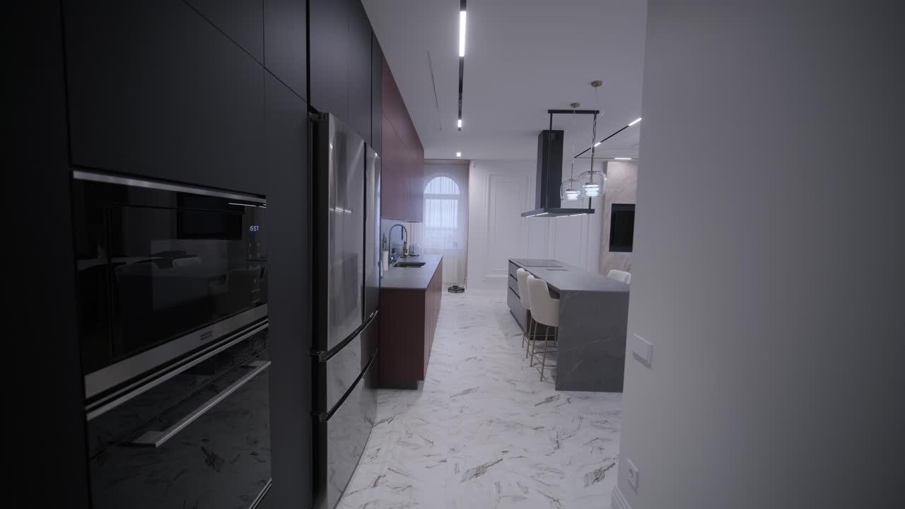 Spacious open-plan kitchen with marble island and dining area, featuring modern lighting fixtures, herringbone wood flooring, and teal accent chairs