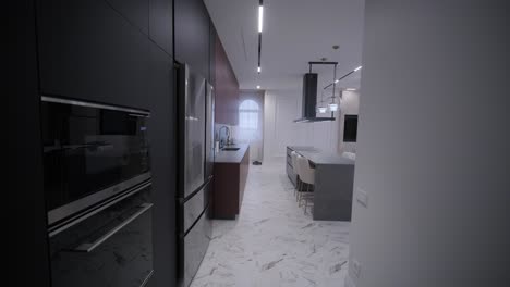 spacious open-plan kitchen with marble island and dining area, featuring modern lighting fixtures, herringbone wood flooring, and teal accent chairs