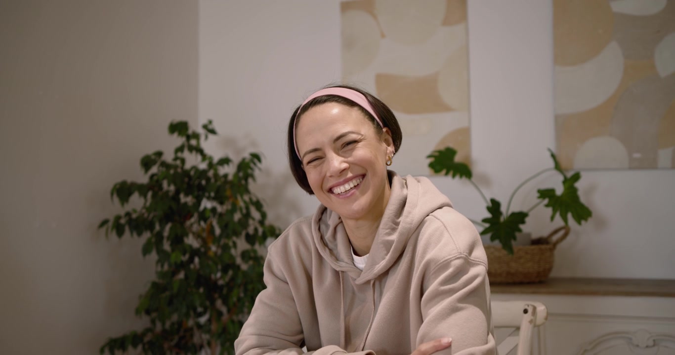 Donna afroamericana a un tavolo di legno che si gira, sorridendo mentre la telecamera si muove mostrando uno smartwatch.