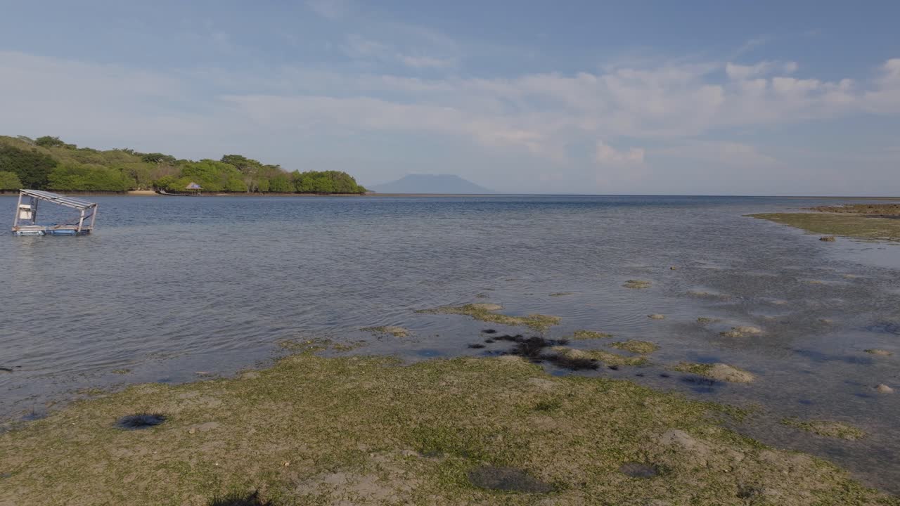Vista de drone em ângulo baixo sobre uma lagoa rasa no Parque Nacional de Bali Ocidental, com a Ilha Menjangan e vulcões no horizonte, revelando um ecossistema costeiro tropical, águas calmas e uma paisagem marítima remota da Indonésia.