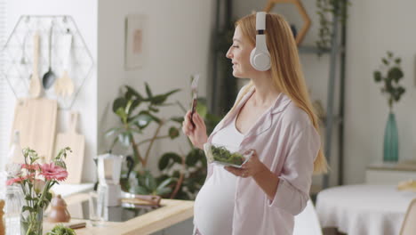 pregnant woman enjoying a salad while listening to music in the kitchen