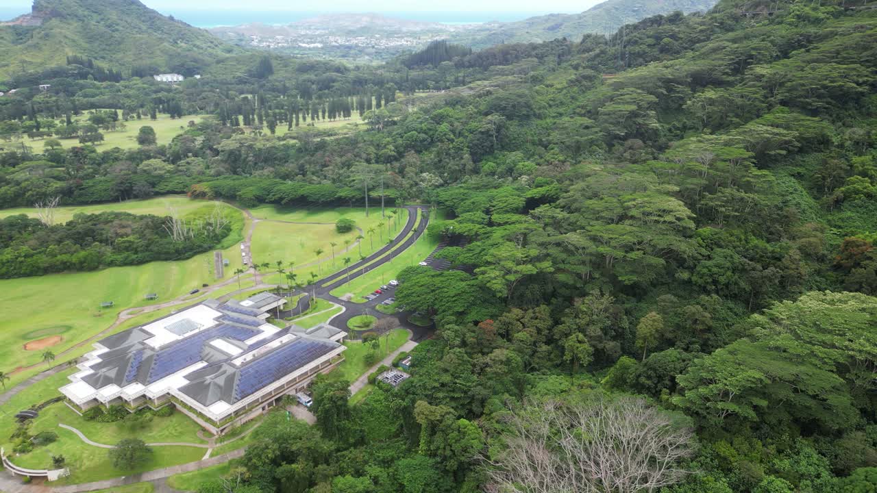 Drone approaches a golf center surrounded by forest and mountains on Big Island, Hawaii.