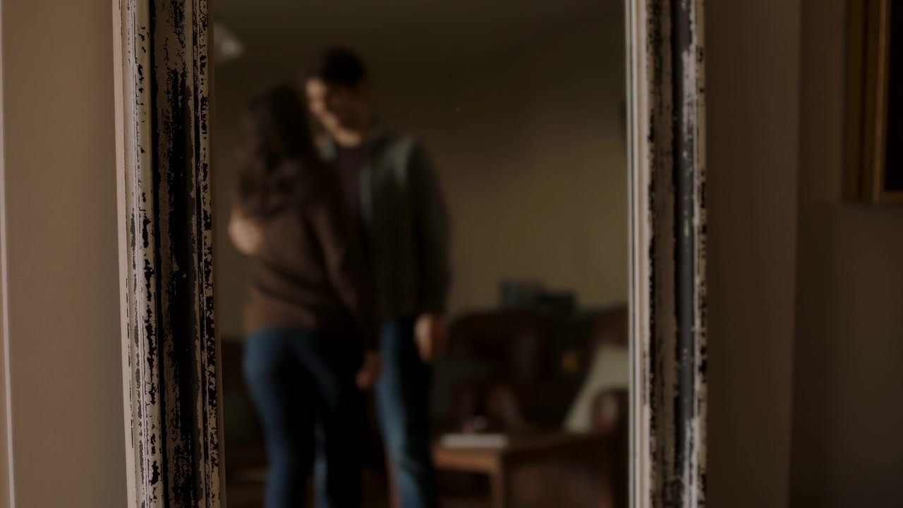 Reflexo borrado no espelho de um casal se abraçando, com iluminação suave e quente, moldura vintage e fundo de sala de estar.