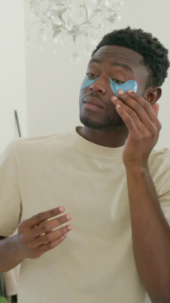 Vertical video: Holding pad, man in tee putting blue gel eye pads at home for care, partner fixing