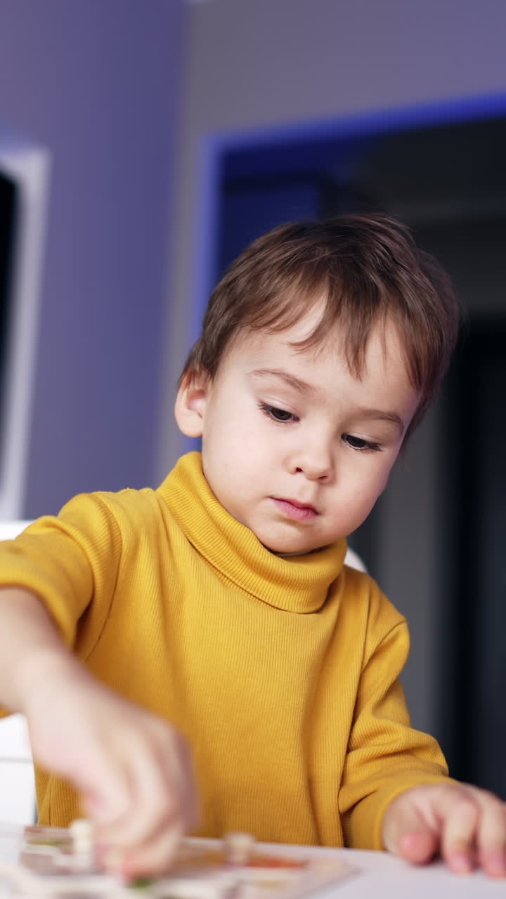 Un adorabile bambino con un maglione giallo è concentrato su un puzzle. Bambino che gioca e studia a casa. Video verticale