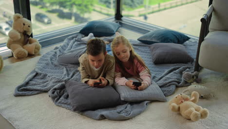 Siblings-using-smartphones-home.-Nice-kids-gaming-mobile-phones.