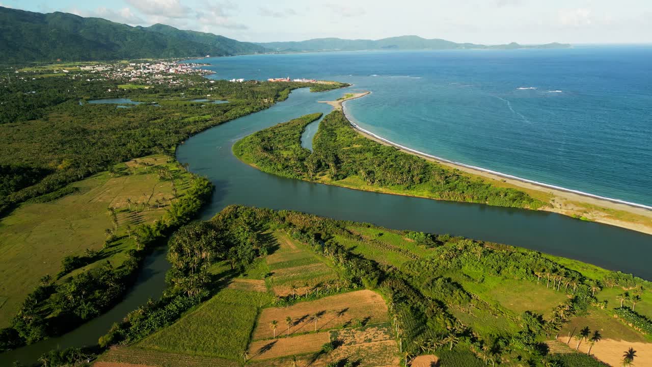Aerial forward shot of river mouth amid lush, verdant tropical fields and island coastline - Virac, Catanduanes, Philippines