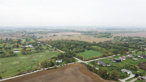 加拿大安大略省佩勒姆市 (pelham, ontario) 郊区的空中高空景观,十字路口,周围是当地房屋,绿色高尔夫球场和广<unk>的农业土地,地平线上有云彩.