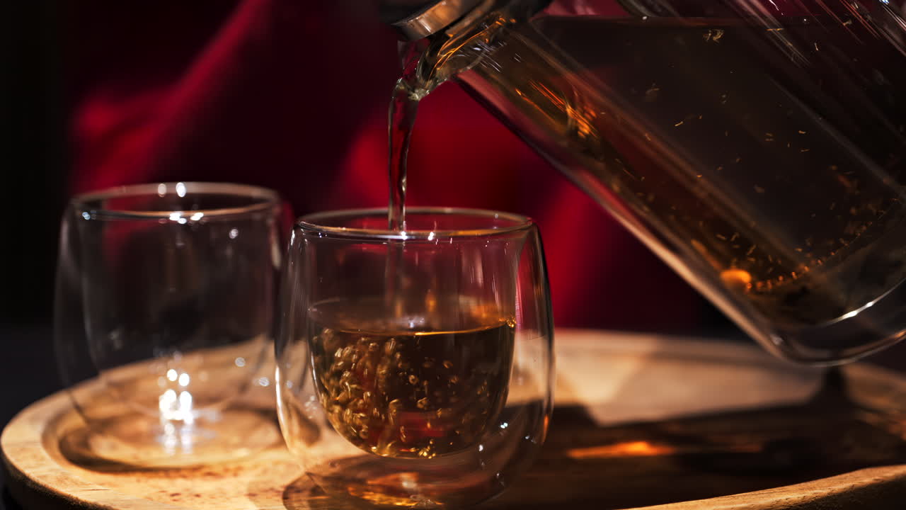Close up of a woman pouring tea from a French press into a double glass cup at a restaurant