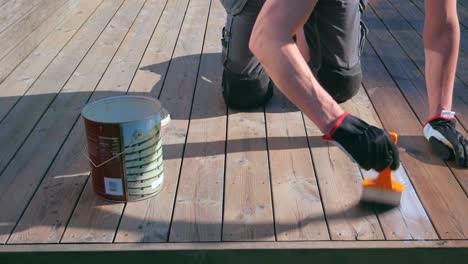 hombre con ropa de trabajo tratando la cubierta de madera con aceite de cubierta