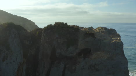 Aerial-drone-shot-of-sea-waves-crashing-in-the-day-time-with-rocky-mountain-in-the-background