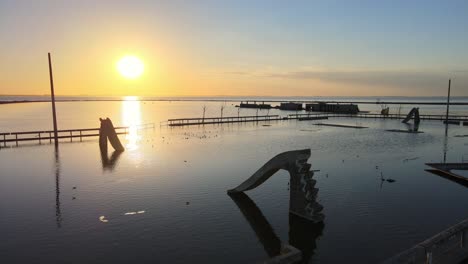 洪水後,在epecuen別<unk>的熱門游泳池和泳池邊滑梯的廢墟,背景是發光的日落,在水面上有美麗的反射,空中拍攝