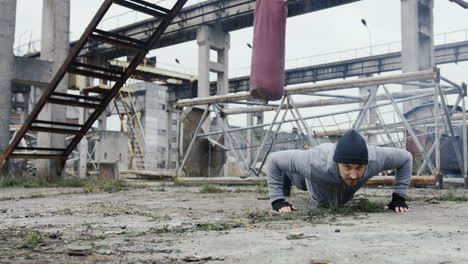 guapo boxeador masculino haciendo flexiones antes de entrenar boxeo al aire libre en la fábrica abandonada en una mañana nublada