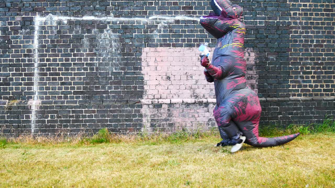 Kostum dinosaurus prasejarah yang ceria berlari dengan pistol gelembung di depan dinding bata.
