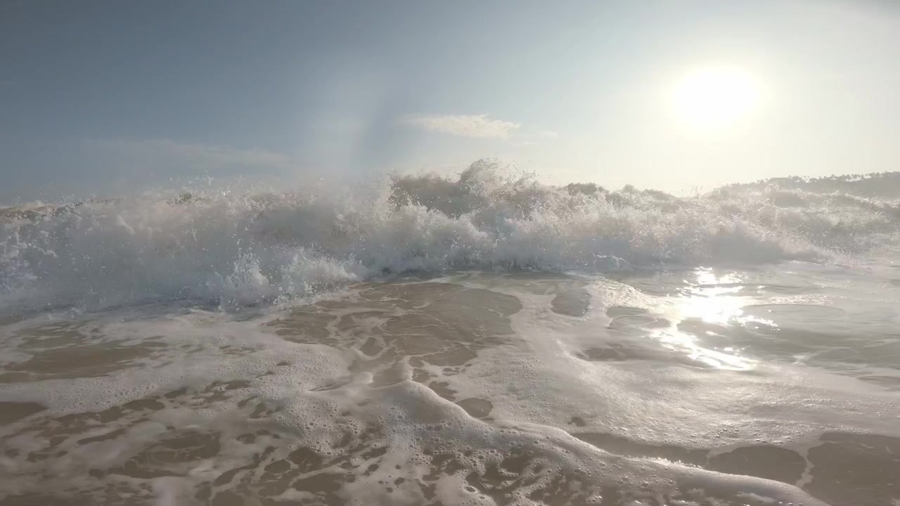 A static waterline view captures a backlit swell rising beneath the sun before its foamy crest breaks into spray, with a distant headland on the horizon in Mirissa, Sri Lanka.