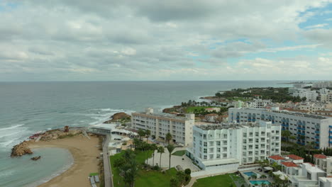 Aerial-Rising-Above-Empty-Pernera-P-Beach-and-Pola-Costa-Beach-Hotel-Apts-on-Cloudy-Day-in-Paralimni-City,-Cyprus