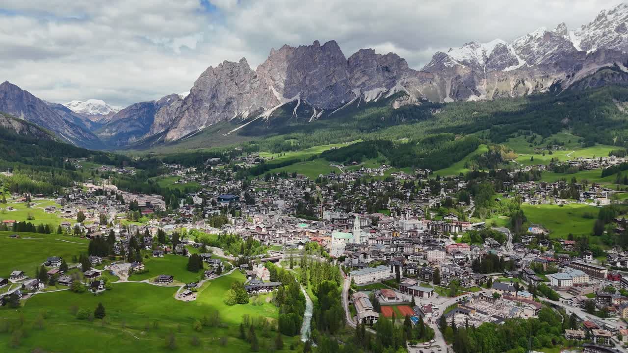 Mountain town surrounded by Dolomites in Ampezzo Valley filmed by drone