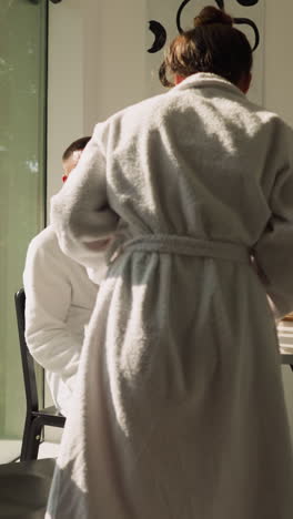 woman joins man sitting at kitchen table. girlfriend in terry bathrobe comes to boyfriend sitting at table to share morning tea together. morning routine