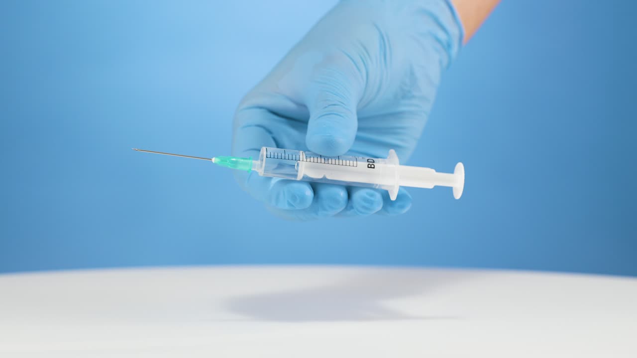 Doctor's hand with gloves shows a plastic syringe isolated blue background