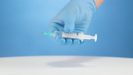 Doctor&#039;s hand with gloves shows a plastic syringe isolated blue background