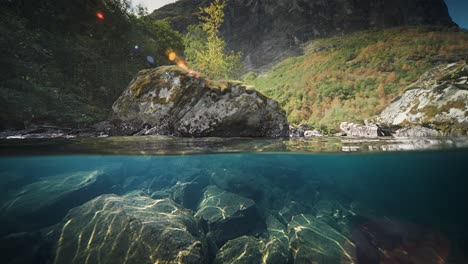 slow motion shot of rocky underwater of loen lake in vestland, norway with mountain range in the background on a sunny day