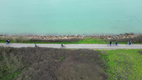 people riding bicycles near ocean shore in loix village in île de ré island france, aerial orbit around shot