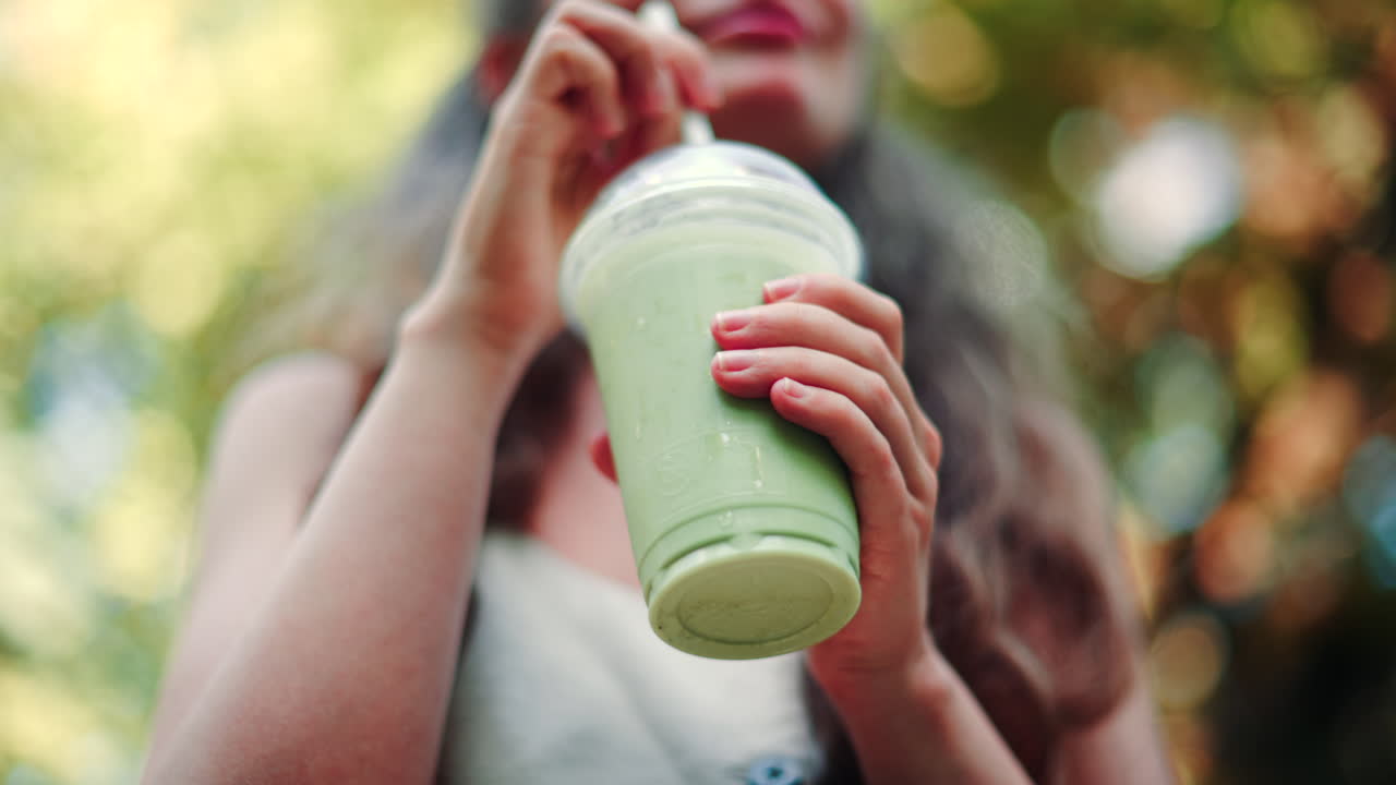 Stylish young woman sipping an iced matcha outdoors, in a park