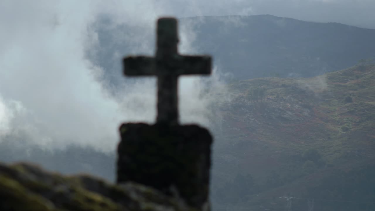 The silhouette of a cross on top of a church overlooking a cloudy mountain range in a 4K timelapse