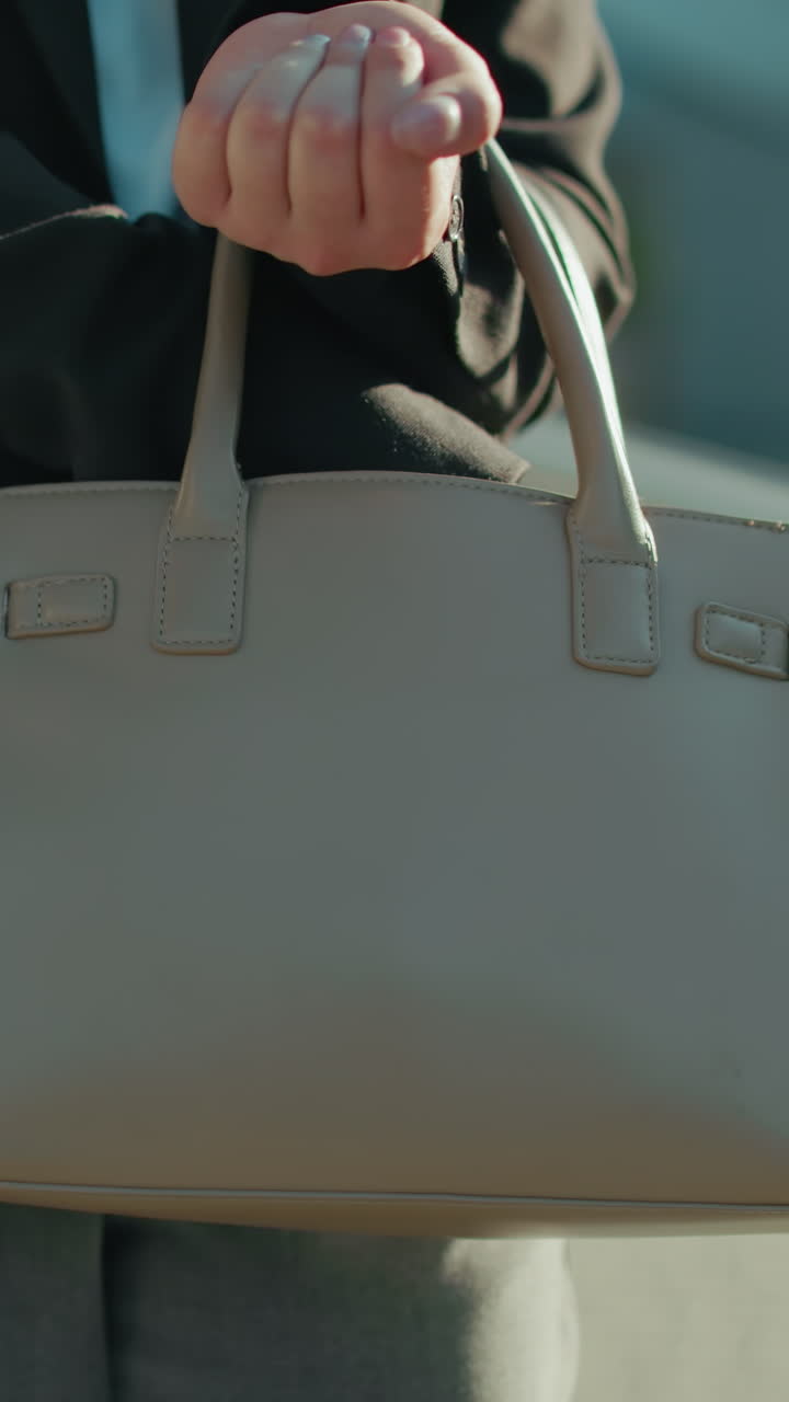 Professional lady struggles to retrieve something from handbag while getting keys, close up of elegant bag and attire, standing near metal railings in sunlit area