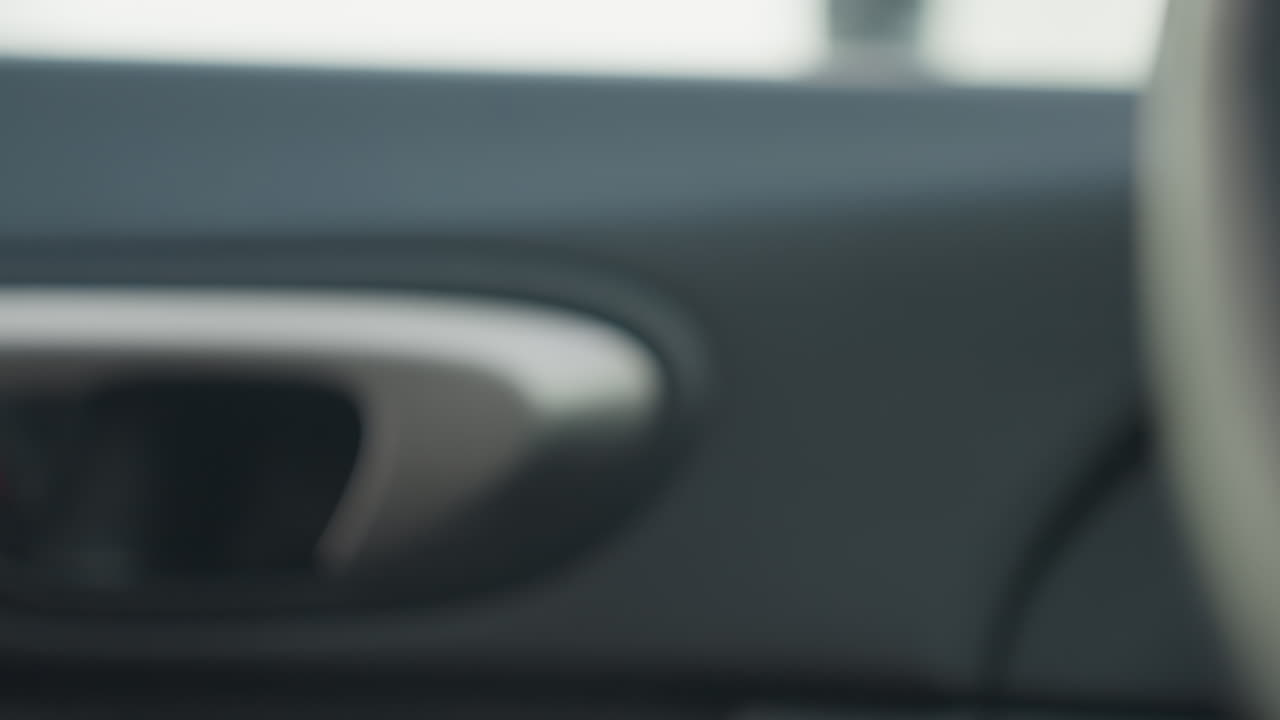 close up fair skinned hand reaching toward car interior door handle to open door while small airborne particles float into vehicle with background elements softly blurred under natural light