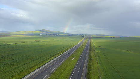 highway through green fields with rainbow