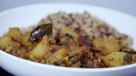 Optisch-Ansprechende-Aufnahme-Von-Papaya-Curry,-Das-Auf-Einer-Platte-In-Einem-Weißen-Gericht-Rotiert,-Mit-Sichtbarem-Quinoa-Und-Chili-Sowie-Lorbeerblättern