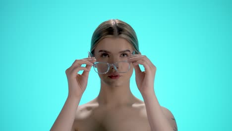 Medium-shot-of-a-young-pretty-woman-putting-on-glasses-to-see-better-with-her-eyes-in-front-of-a-turquoise-background-in-slow-motion