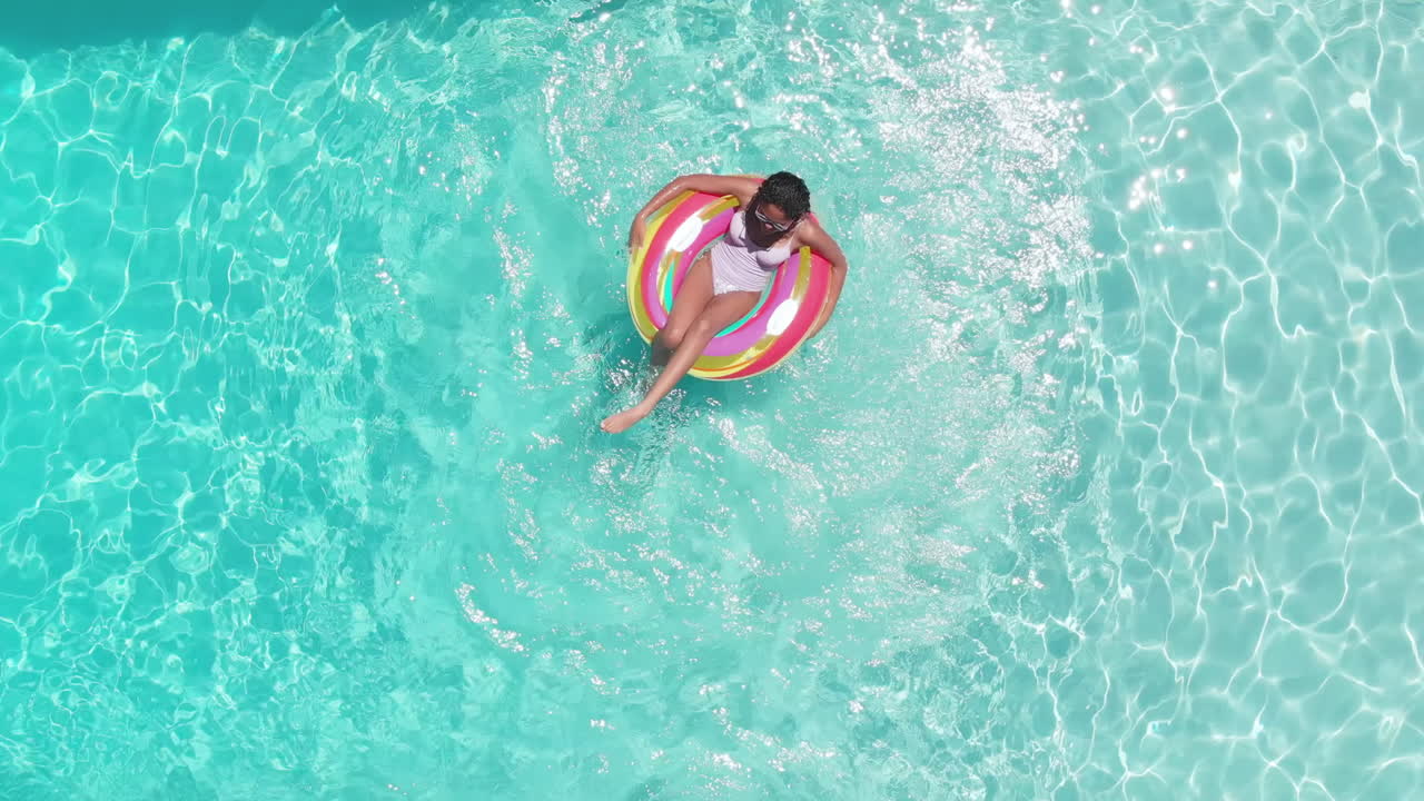Aerial of happy african american teenage girl playing on inflatable in sunny pool, copy space