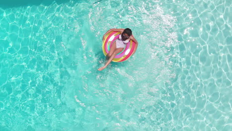 Antena-De-Una-Feliz-Adolescente-Afroamericana-Jugando-En-Inflable-En-Una-Piscina-Soleada,-Espacio-De-Copia