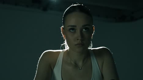 medium shot of a fit woman cycling indoors, showing a concentrated face as the camera moves smoothly from one side profile across the front to the other side, revealing emotion, flow, and strength