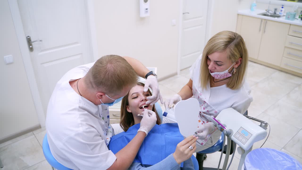 Dentistry concept. Assistant holds artificial teeth. Stomatologist selecting tooth implant for female patient in modern dentist office.