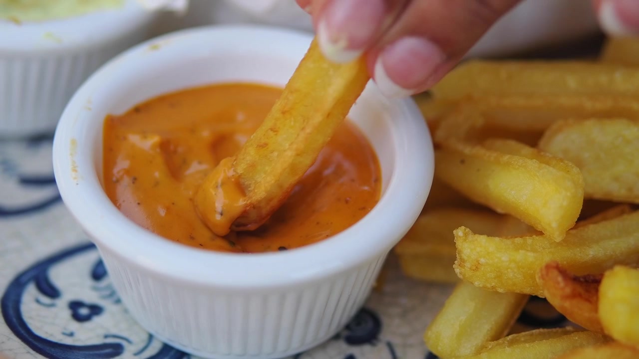 Hand Dipping a French Fry into Orange Sauce