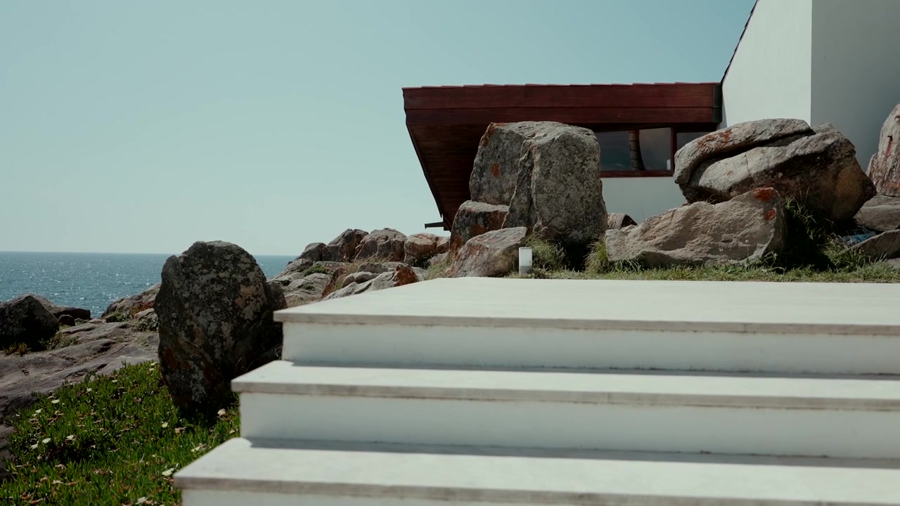 Gradini in cemento che conducono a una casa moderna accanto a rocce, con vista sulla costa oceanica.