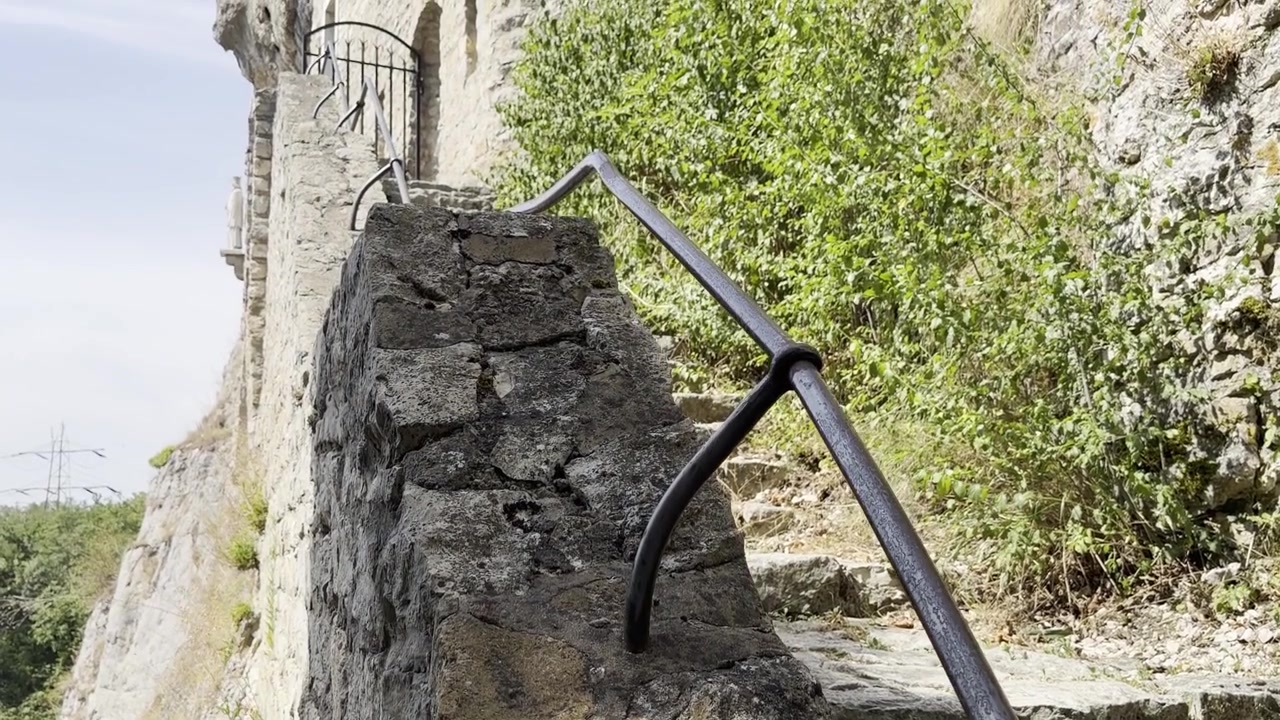 Um lento movimento de inclinação para cima segue a histórica escadaria de pedra, o corrimão de ferro e a entrada da capela construídos nas falésias de calcário de Isteiner Klotz