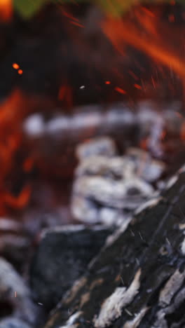 smoldering charcoals in grill. wooden stick turning over smoldered logs in fire. burning wood in fire. sparks in fire over smoldered logs. close-up. vertical video