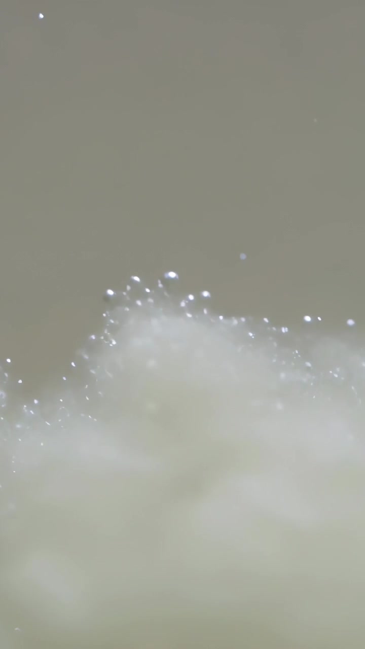 Video verticale: Luce cangiante, bolle di schiuma che formano una cresta in una ciotola (macro), mostrando una pellicola d'acqua luminosa.