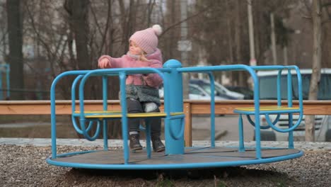 lonely little kid girl spinning on a carousel at children's playground