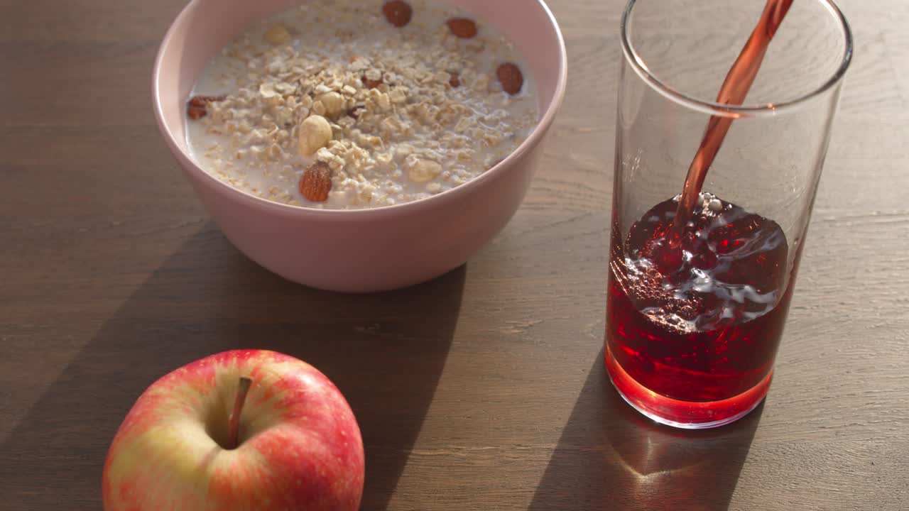 Colazione salutare con una ciotola di avena, una mela e succo versato.