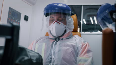 exhausted paramedic riding ambulance with colleague low angle of tired male doctor taking off face shield and mask and breathing in exhaustion while riding emergency medicine vehicle with coworker together