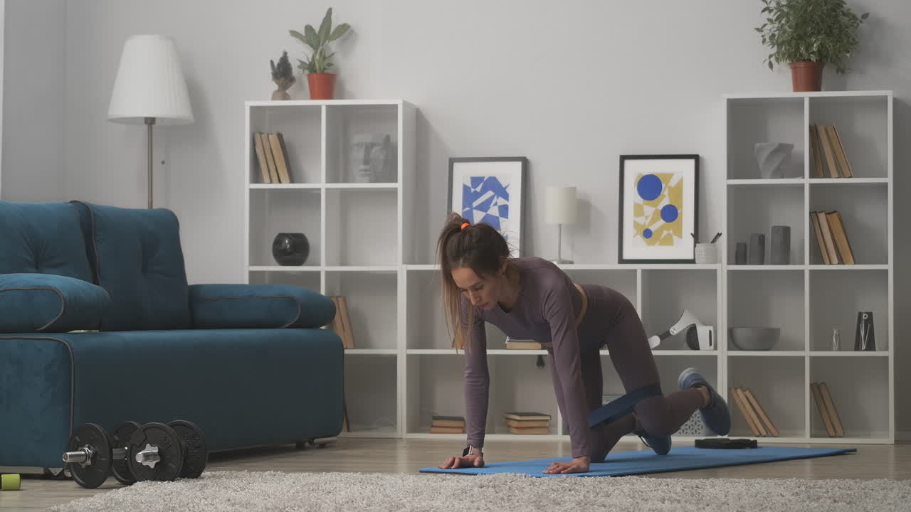 joven sexy está entrenando culo y piernas haciendo ejercicios con banda elástica de fitness entrenamiento en casa para estar en buena forma de pie de manos y rodillas en la habitación