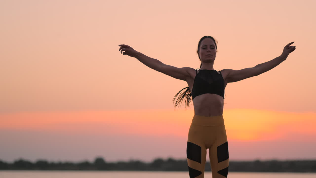 una mujer haciendo ejercicios en la playa. una entrenadora de cabello oscuro en una camiseta corta deportiva y leggings de gimnasio hace ejercicios deportivos y salta en un día de verano en una puesta de sol en la playa