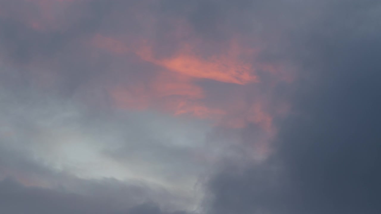 Bandas de nubes rosadas iluminadas flotan sobre una capa gris más oscura mientras la luz se desvanece al final del día