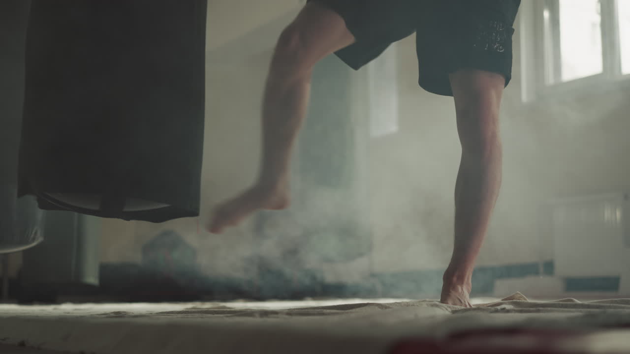 Sportsman jumps kicking punching bag in sports club closeup. Professional kick-boxer exercises with heavy equipment in gym slow motion. Martial arts