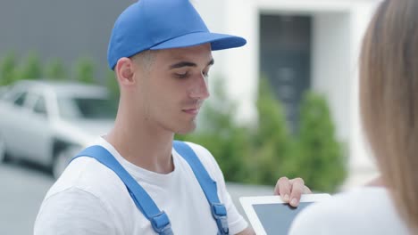 beautiful woman meets a delivery man who gives her a parcel box beside her home, she signs electronic signature on tablet. concept of courier, home delivery, online shopping